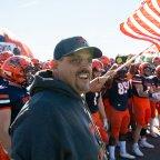 Coach Blaise Faggiano stands ahead of football players waving Pioneers flag