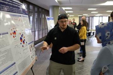 A student makes a presentation beside a poster at the 2024 学生 Conference for 研究, Professional Activities, 及创意艺术