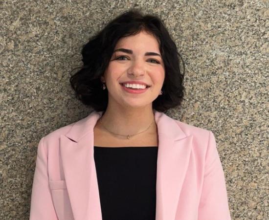 Grace VanEtten '27 in black top and pink blazer, stands against a stone wall.