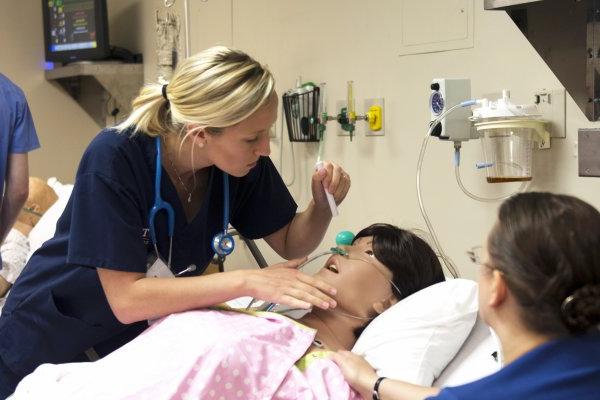 护理 students in a lab simulation look over a mannequin in a hospital bed.