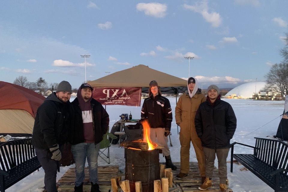 Members of AXP stand out int he cold by a fire. 