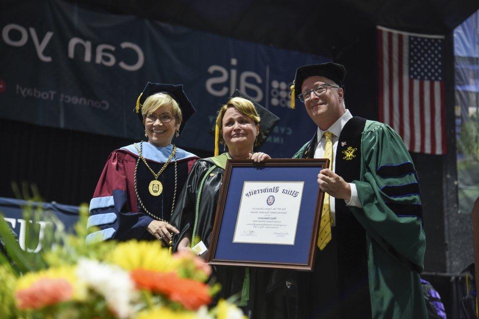 Professor of Occupational Therapy Mary Siniscaro stands between Provost 托德Pfannestiel and President Laura Casamento, holding her award at the 2023 Undergraduate Commencement Ceremony.