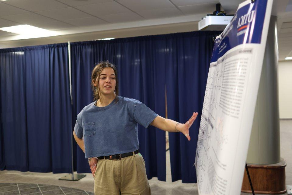 A student makes a presentation beside a poster at the 2024 学生 Conference for 研究, Professional Activities, 及创意艺术